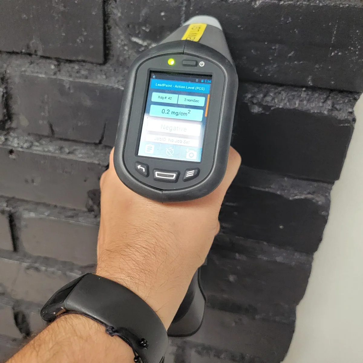 The X-ray fluorescence analyzer held against a painted brick wall, reading in progress